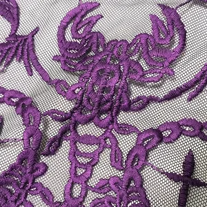 Macro detail of deep purple scorpion embroidery on delicate black mesh lace fabric patch