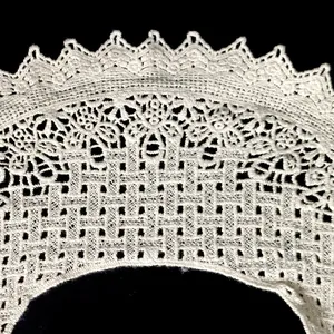 Macro detail of intricate hollowed-out floral embroidery on white cotton lace collar