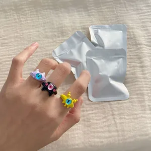 Detailed view of three colorful cute monster animal rings worn on a hand with packaging bags