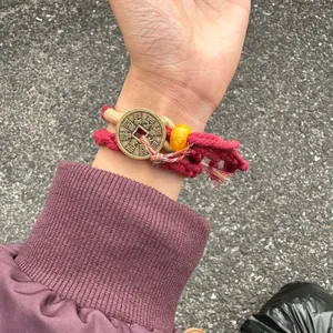 Close-up detail of a hand-woven ethnic red bracelet with a brass coin and yellow bead