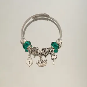 Close-up of a silver-toned cable bracelet featuring green beads and heart crown charms