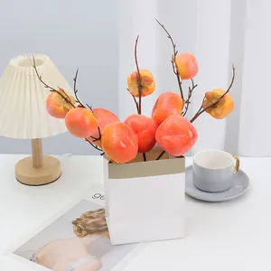 Détail de branche de kaki artificiel avec fruits en mousse orange pour décoration maison.