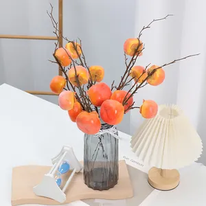 Détail de branche de kaki artificiel avec fruits orange vif et tiges réalistes dans un vase en verre.