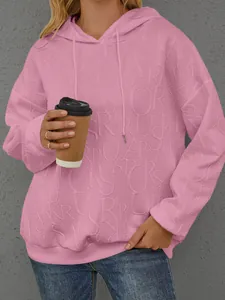Detailansicht eines rosa Damen Kapuzensweatshirts mit 3D geprägter Buchstabenstruktur.