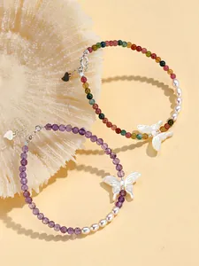 Macro view of shell butterfly charm on purple amethyst and freshwater pearl beaded bracelet.