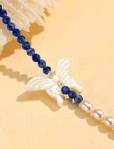 Macro view of a blue crystal bead and white butterfly pearl necklace design detail.