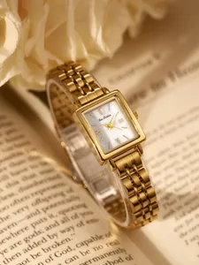 Elegant gold-toned rectangular women's watch with vintage metal link strap on a book