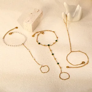 Détail de bracelets de doigt dorés avec perles, cœurs verts et chaînes fines minimalistes