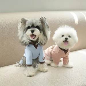 Two small dogs wearing blue and pink soft cotton four-legged home wear onesies on a sofa