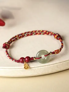 Gros plan d'un bracelet en corde rouge avec un anneau en jade vert et des breloques dorées.