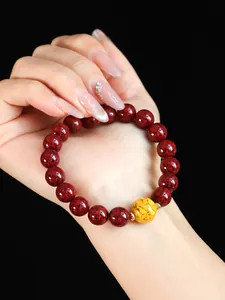 Detail eines natürlichen roten Zinnober-Armbands mit goldener Perle am Handgelenk