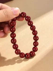 Nahaufnahme eines natürlichen roten Zinnoberperlenarmbands, das von einer Hand gehalten wird