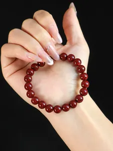 Detailansicht eines Armbands aus rotem Zinnober, gehalten von einer gepflegten Hand.