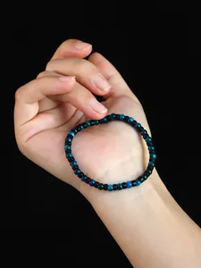 Primer plano de una pulsera de 4mm de ojo de tigre azul sostenida en mano sobre fondo negro