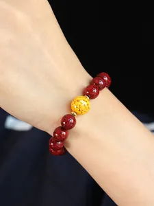 Nahaufnahme eines roten Zinnober-Armbands mit einer goldfarbenen Mittelperle