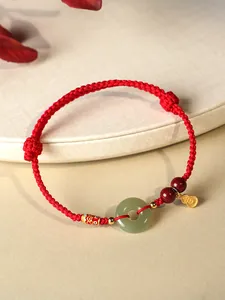 Gros plan d'un bracelet tressé rouge avec beignet de jade, perles de cinabre et breloques.