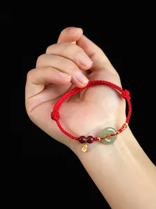Détail d'un bracelet en corde rouge fait main avec jade et breloque koi dorée