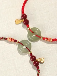 Gros plan d'un bracelet en cordon rouge fait main avec jade et breloques dorées.