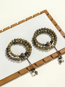 Detailed view of green sandalwood double-loop beaded bracelet with engraved charms and tassels