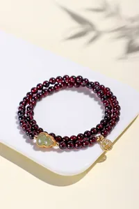 Detail des Granat-Armbands mit Jade-Kalebasse und goldenem Segensanhänger im Fokus.