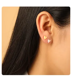 Close-up van minimalistische roze en gele hart keramische oorknopjes op een oor