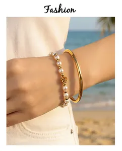 Close-up of minimalist gold titanium steel bangle and pearl bracelet set on wrist
