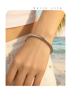 Elegant minimalist silver-toned titanium steel open bangle worn on wrist at sunset beach