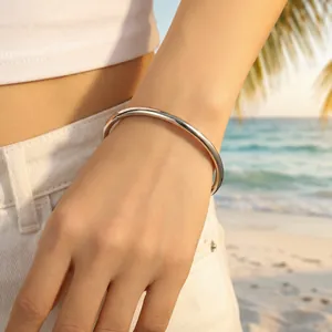 Minimalist silver titanium steel round bangle bracelet shown on a wrist at the beach.