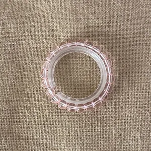 Close-up of pink translucent beaded bracelet on clear ring display with burlap background.
