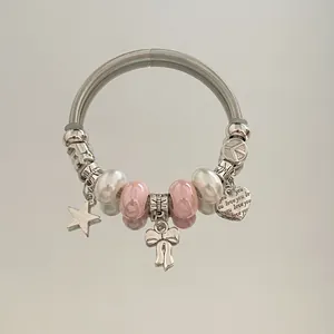 Gros plan d'un bracelet à breloques DIY avec perles roses, pendentifs cœur et nœud