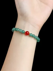 Detailansicht eines Perlenarmbands aus grünem Chalcedon mit rotem Achat-Akzent am Handgelenk.