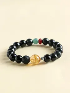 Detail of black obsidian bracelet with yellow crystal and lava stone on beige background.