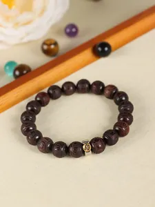 Detailed macro shot of a dark sandalwood beaded bracelet with a carved metallic charm