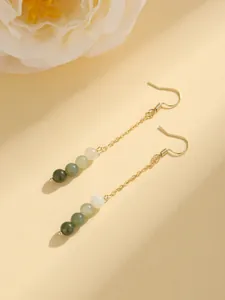 Detail of vintage gold dangle earrings with gradient green and white beads on beige background.