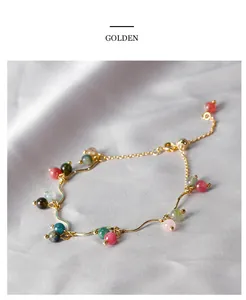 Dettaglio di bracciale con pietre preziose colorate e filo dorato ondulato su seta.
