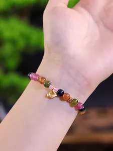 Detalle de pulsera de cuentas de turmalina de colores con amuleto de candado dorado.