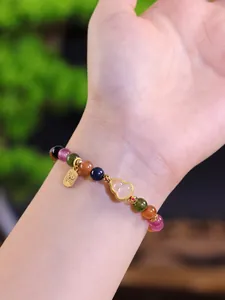 Primer plano de pulsera de cuentas de turmalina multicolor con dije de oro y jade de calabaza.