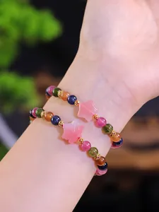 Detalle de una pulsera de cuentas multicolores con dije de hoja de arce rosa en muñeca