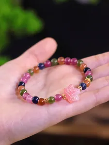 Detalle de pulsera de cuentas de turmalina de colores con colgante de flor rosa.