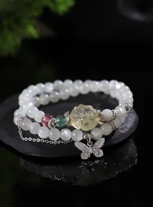 Primer plano de una pulsera de perlas de piedra de luna con un dije de mariposa plata.
