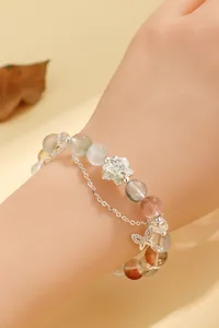 Dettaglio di un bracciale di perle in stile cinese con ciondoli a loto e farfalla