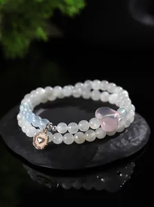 Primer plano de una pulsera de piedra de luna de dos hilos con dije de corazón rosa