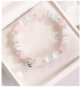Detalle de pulsera de piedra ojo de gato con cuentas rosas y dije de cascabel plateado.
