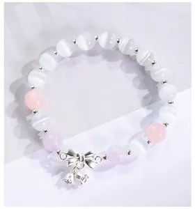 Detalle de pulsera de cuentas de ojo de gato blancas con cuentas rosas y dije de lazo.