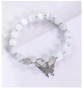 Detalle de pulsera de cuentas de ojo de gato con dijes de mariposa y luna blanca.