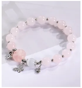 Detalle de pulsera de cuentas rosas con dije de mariposa y piedra de ojo de gato