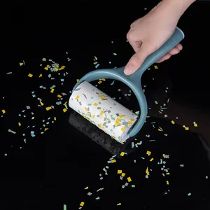 Handheld sticky lint roller brush removing colorful confetti on a dark reflective surface