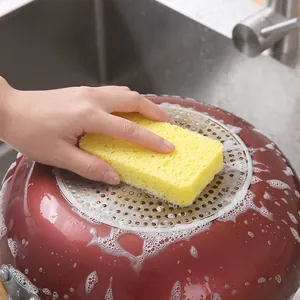 Yellow wood pulp sponge scrubbing oil stains on a cooking pot bottom in a kitchen sink