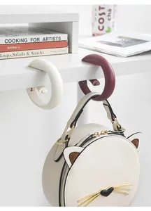 Portable ring-shaped desk bag hook clipped to a white table edge with a hanging bag