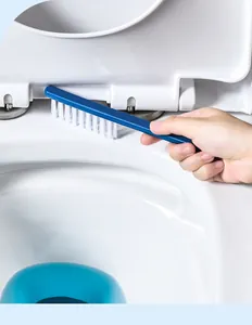 Close-up of a blue long-handle gap cleaning brush scrubbing a toilet seat hinge